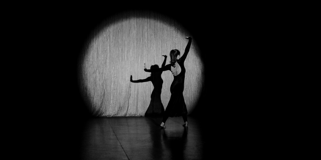 Ballet dancer in a black gala dress on a stage, lit by a single spotlight (black and white)